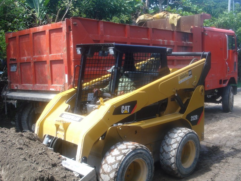 Minicargador CAT junto a camión de volteo cargando material