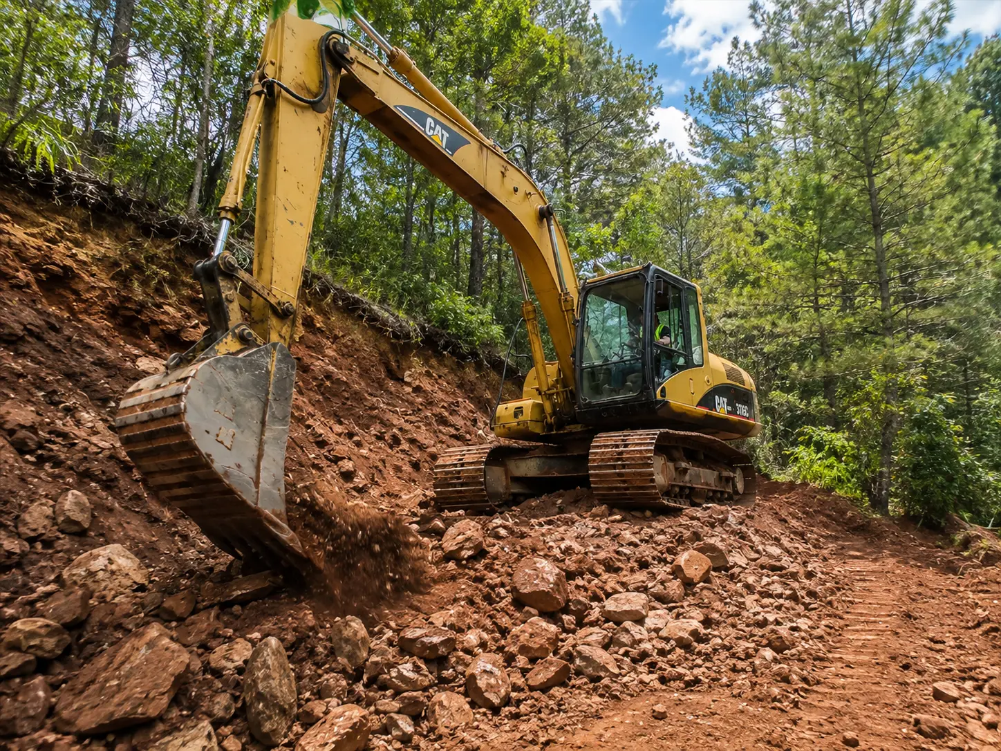 Excavadora cargando tierra y escombros en un camión de volteo durante trabajos de terracería